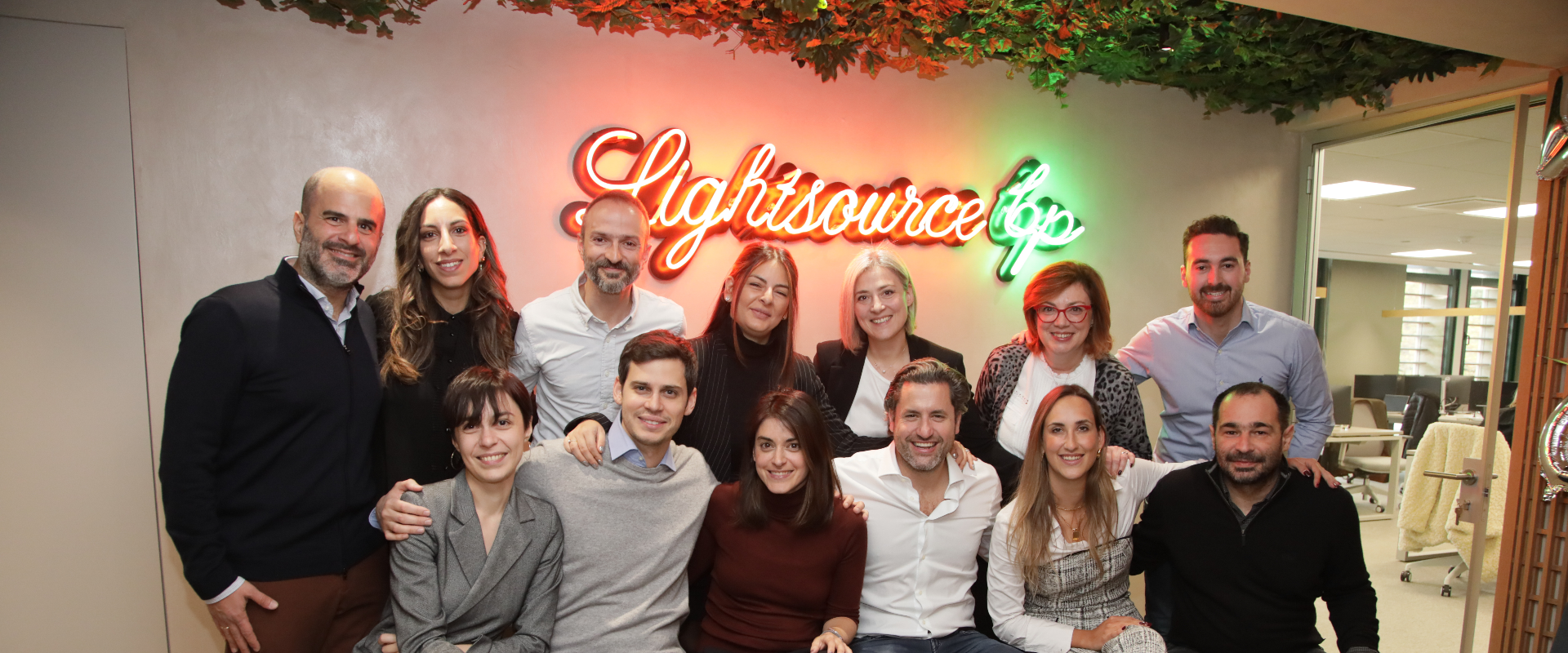 People in office posing in front of neon sign