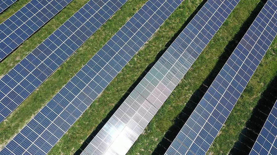 Aerial shot of light reflecting off a field of solar panels with grass growing below